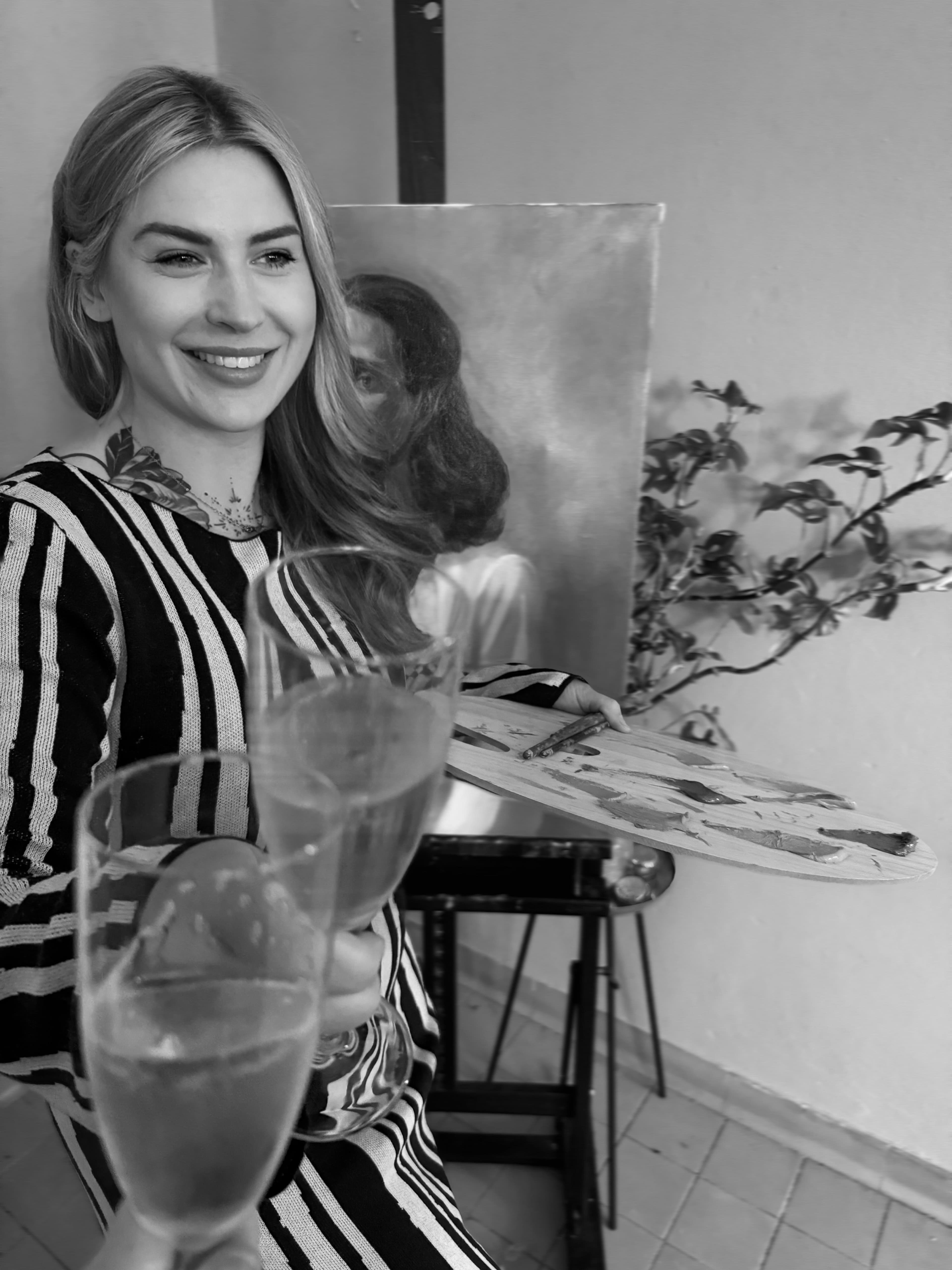 svartvit bild på karin lilja som målar och skålar med ett champagneglas